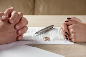 a couples hand on top of a divorce paper with pen and wedding rings in the center